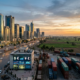 City skyline, highway, cargo trains, containers, and sign displaying $ € ¥ £